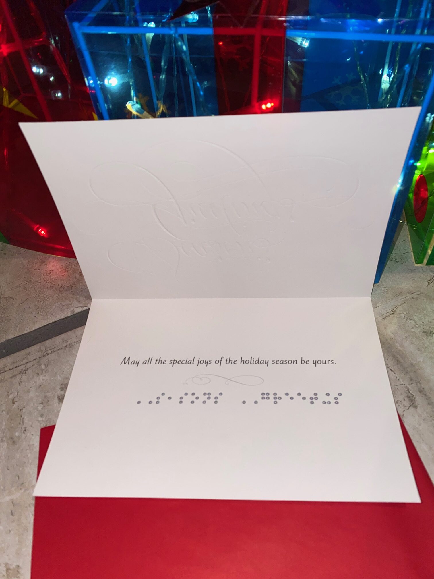 White Christmas greeting card opened to reveal printed holiday message with Braille embossed beneath the text.
